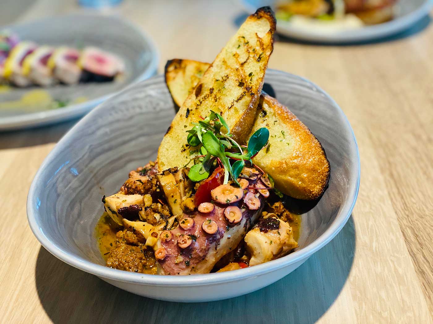 spanish stye braised octopus with grilled toast in a gray bowl