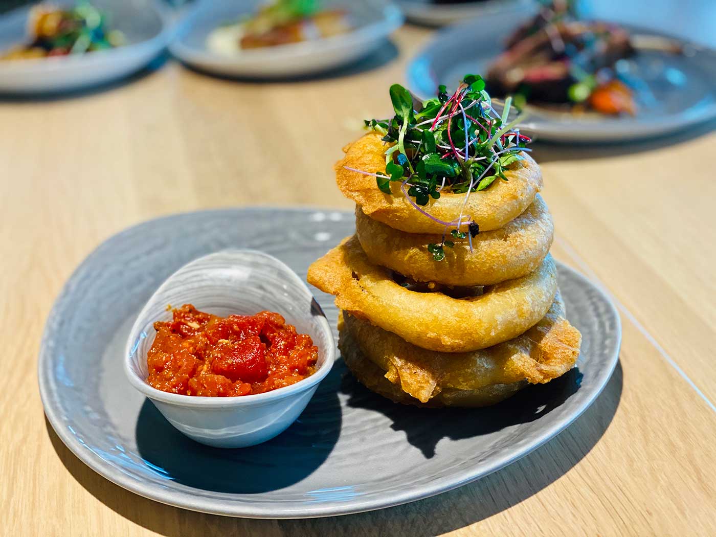 Vidalia onion rings in a stack with side of tomato sauce on a gray plate